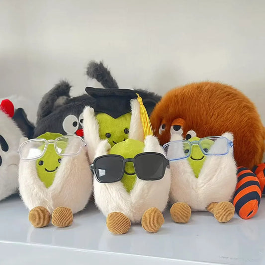 Jellycat pistachio. Plush toys resembling llamas with glasses and a spider on a white surface