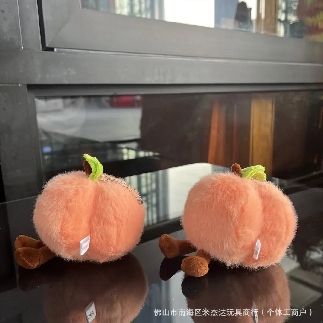Jellycat. Two plush pumpkin toys on a reflective surface with a blurred background
