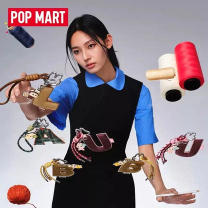 Labubu Pin for Love. Woman holding various keychains with colorful spools of thread in the background, featuring the Pop Mart brand.