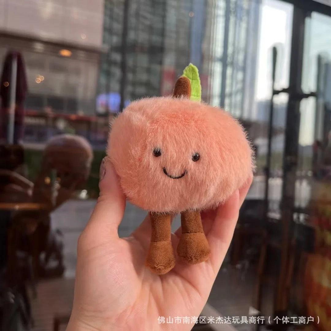 Jellycat. Plush toy resembling a peach held in a hand with a blurred indoor background