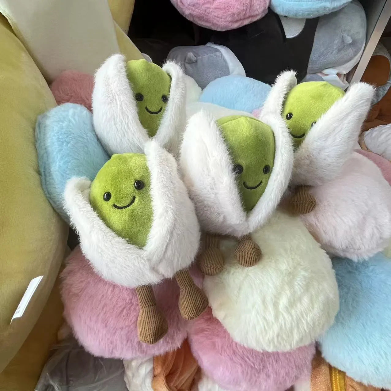 Jellycat pistachio. Plush toys shaped like green characters with white sleeves in various colors.