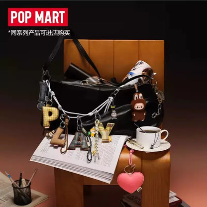 Labubu Pin for Love. Black handbag with various keychains on a desk, featuring the Pop Mart brand.