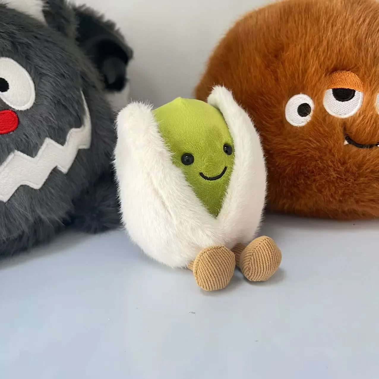 Jellycat pistachio. Plush toy resembling a roll of sushi with a smiling face, surrounded by other plush toys on a light background.
