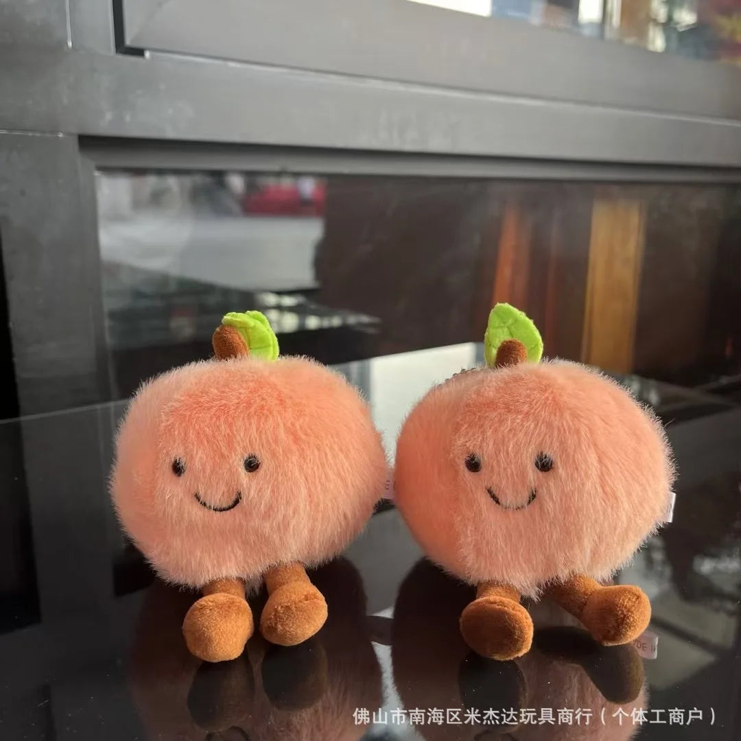 Jellycat. Two plush peach toys with smiling faces on a reflective surface.