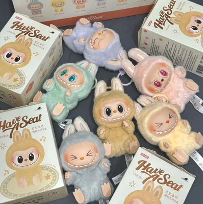 Labubu. Plush toys resembling animals with 'Have A Seat' packaging on a gray surface.
