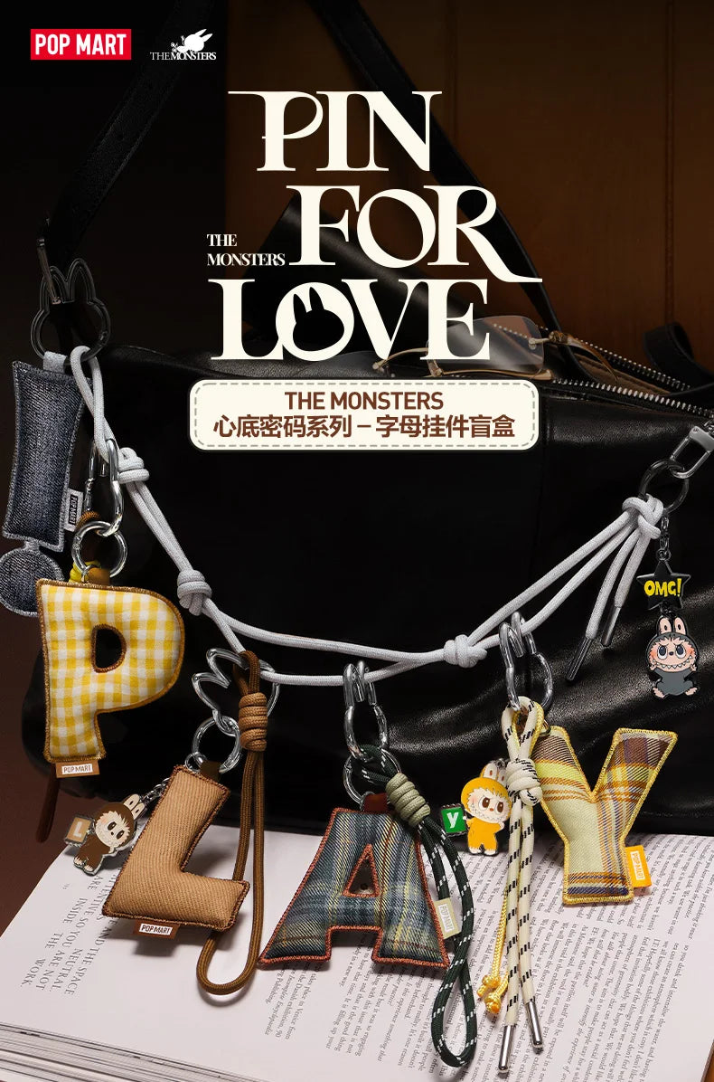 Labubu Pin for Love. Collection of letter-shaped keychains spelling 'PLAY' with a black bag and magazine in the background, featuring the brand 'Pop Mart'.