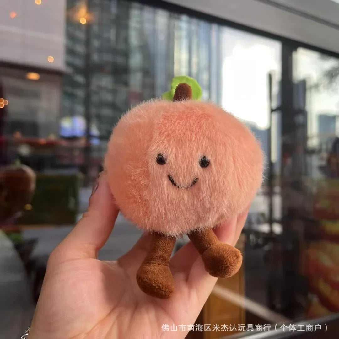 Jellycat. Plush toy resembling a peach held in a hand with a blurred indoor background