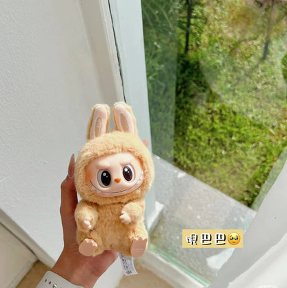 Plush toy Labubu held by a hand with a window and greenery in the background.